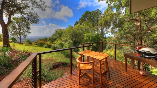 A wooden deck with a table and chair, surrounded by lush greenery and trees.