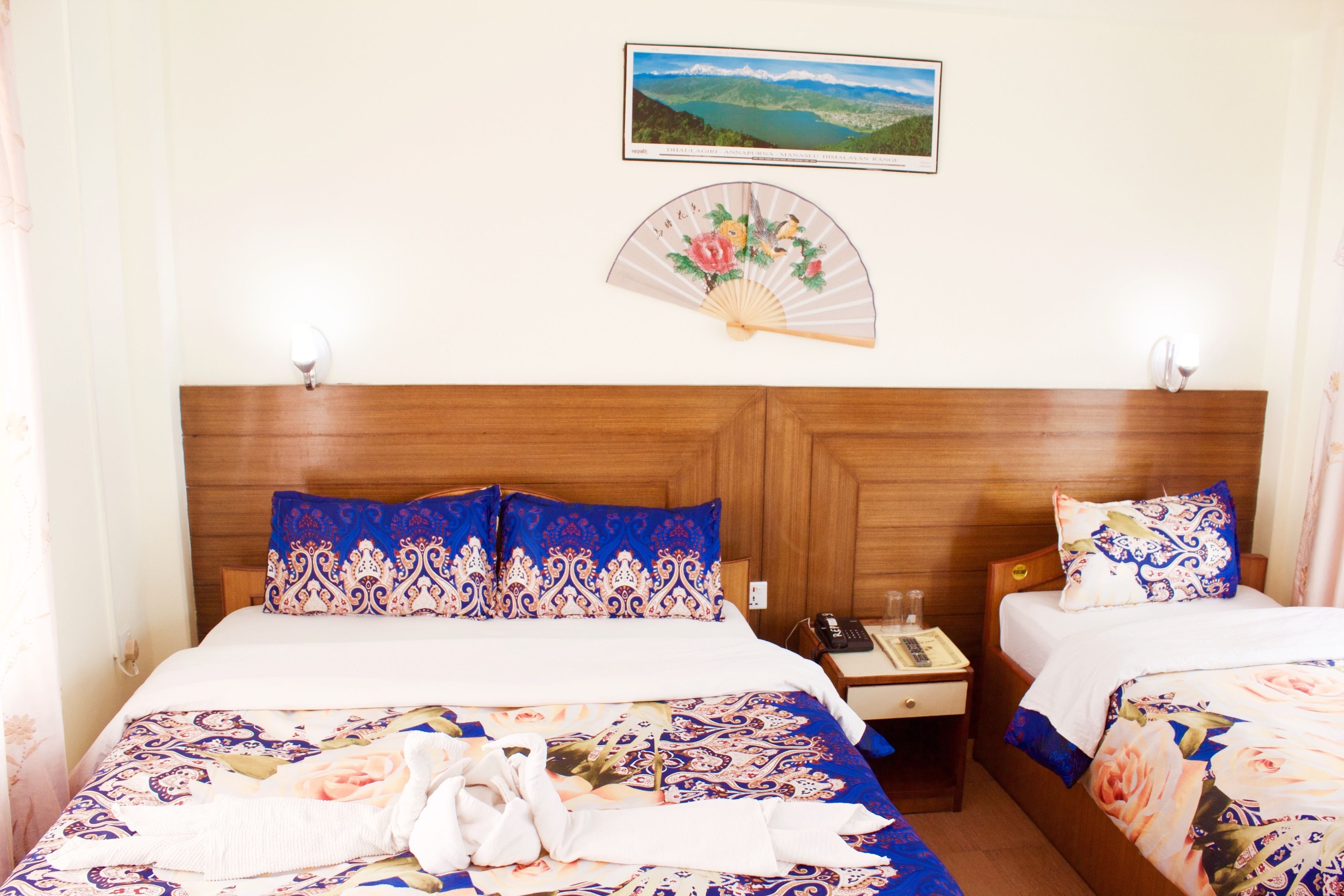 A hotel room with two beds, a wooden headboard, a bedside table with a phone, and a framed landscape picture on the wall.