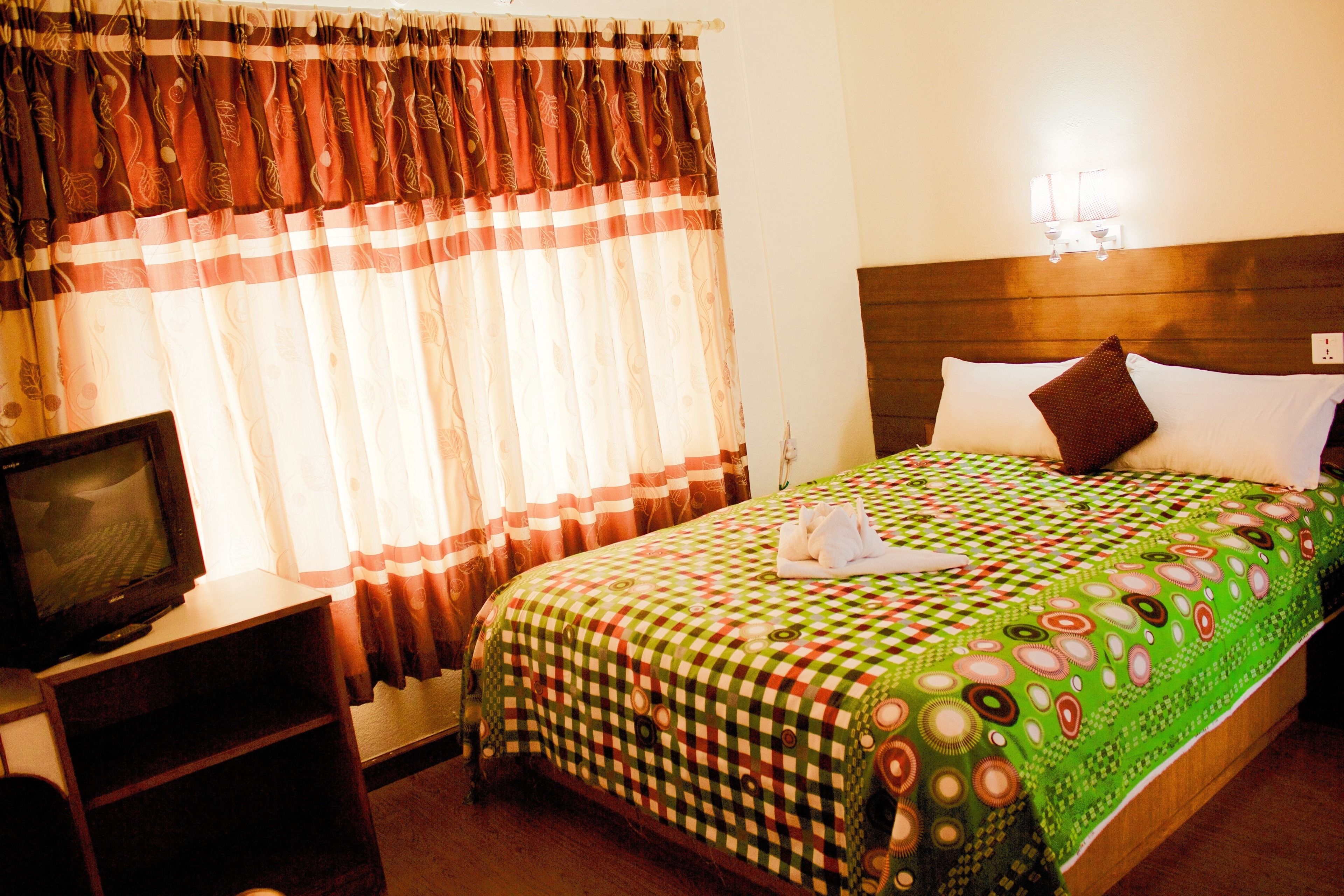 Une chambre d’hôtel avec un lit, un téléviseur posé sur un meuble et des rideaux.