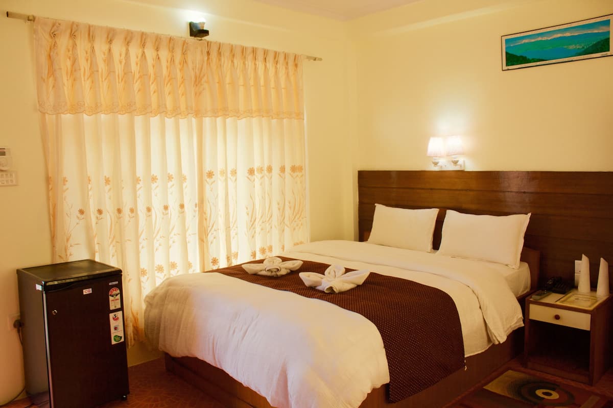 Une chambre d’hôtel avec un lit, une table de chevet, une lampe et un réfrigérateur.