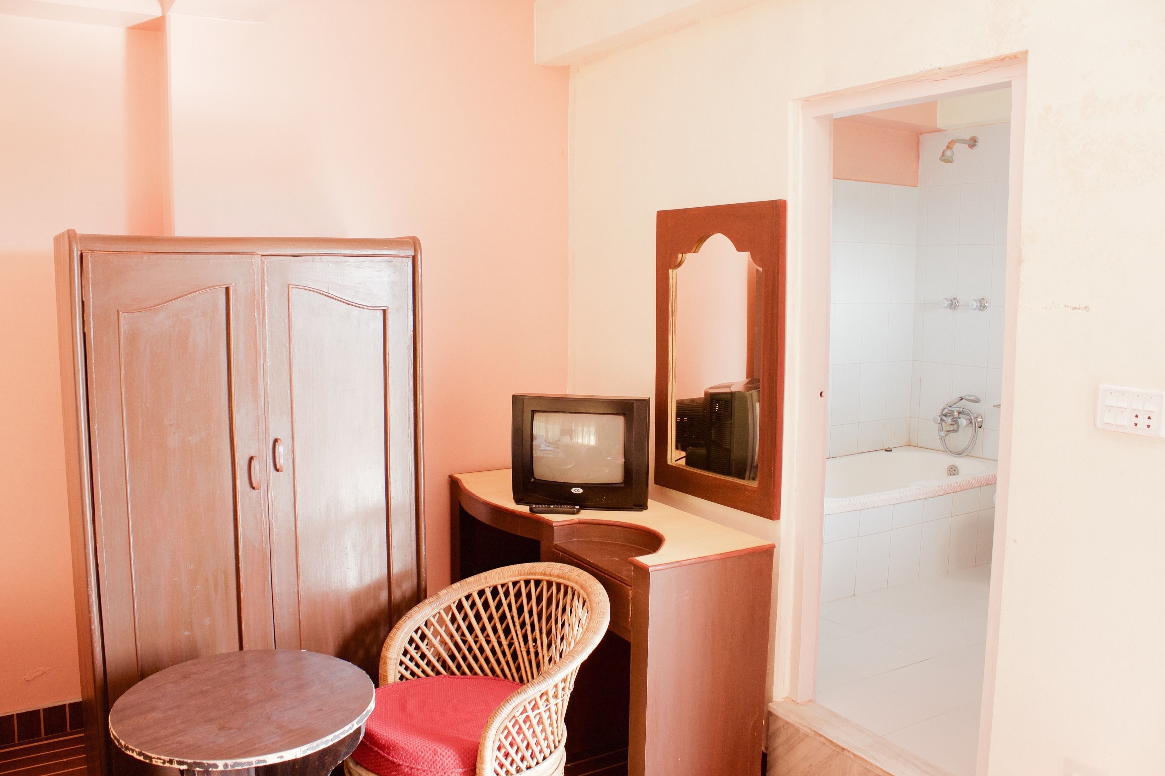 A bathroom with a wooden cabinet, a television, a wicker chair, and a bathtub.