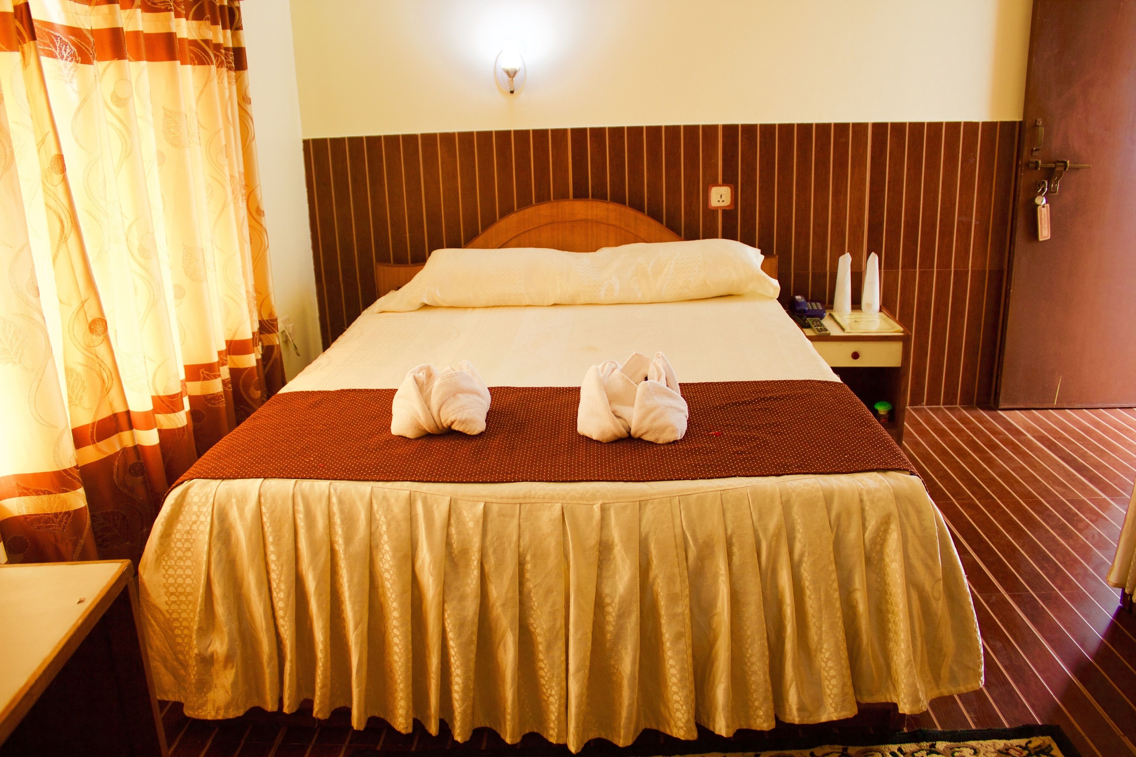 A neatly made bed with a brown headboard, a bedside table with a lamp, and a door with a key lock.