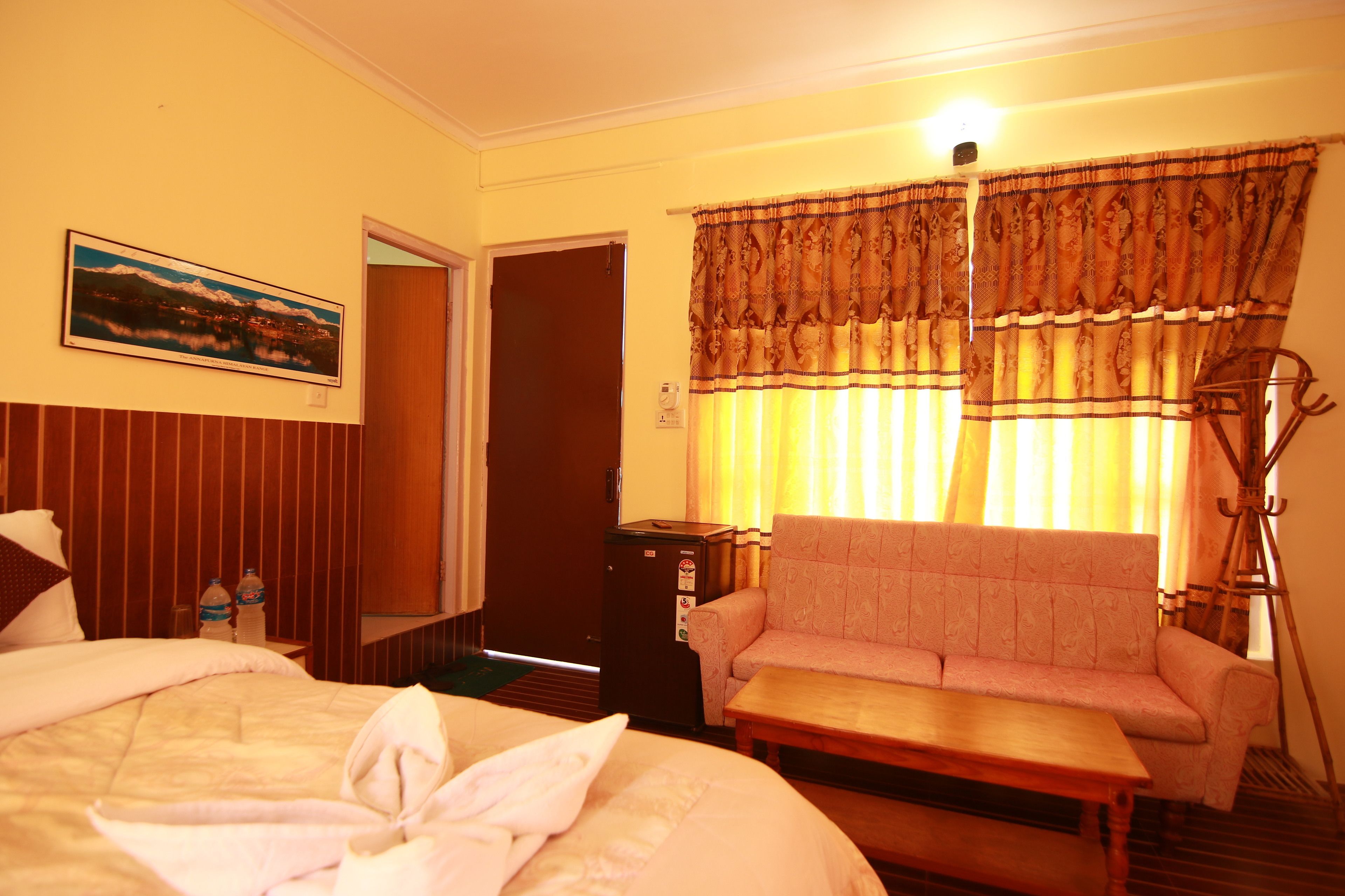 A hotel room with a bed, a sofa, a small table, a coat rack, and a painting on the wall.