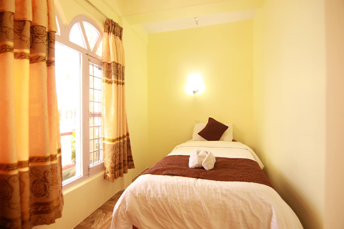 Une chambre d’hôtel avec un lit, des rideaux, une fenêtre et un luminaire fixé au mur.