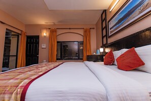 A hotel room with a large bed, a nightstand, a painting on the wall, and a view through the door. - Moonlight Resort and Spa (Pokhara)