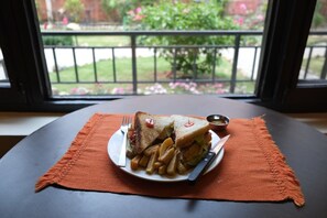 A sandwich and fries on a plate with a fork and knife, placed on an orange placemat. - Moonlight Resort and Spa (Pokhara)