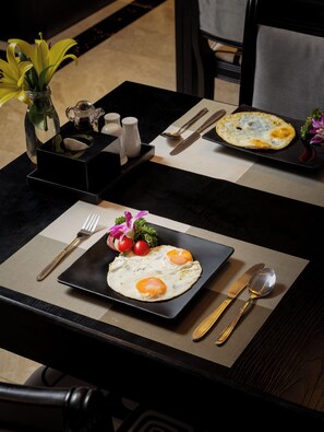 A dining table with a plate of eggs, a vase with flowers, and a salt and pepper set. - Ja Cosmo Premier Hotel (Hanoi)