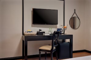 Ein Hotelzimmer mit schwarzem Schreibtisch, Fernseher, Stuhl, kleinem Tisch und Spiegel.