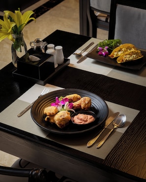 A dining table with a plate of food, cutlery, and a vase with flowers. - Ja Cosmo Premier Hotel (Hanoi)