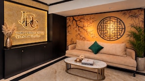 A modern hotel lobby with a large illuminated sign, a sofa with a green pillow, a marble coffee table, and a potted plant. - Ja Cosmo Premier Hotel (Hanoi)