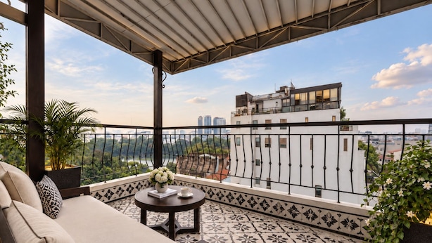A balcony with a sofa, a small table with a vase and book, and a view of a cityscape. - Ja Cosmo Premier Hotel (Hanoi)
