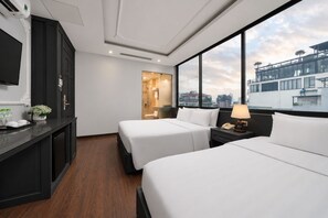 A hotel room with two beds, a desk with a telephone, and a view of the cityscape through large windows. - Ja Cosmo Premier Hotel (Hanoi)