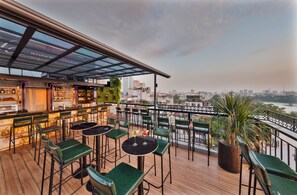 A rooftop bar with outdoor seating, a city view, and a glass ceiling.