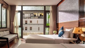 Une chambre d’hôtel avec deux lits, un canapé, un balcon donnant sur une vue agréable et une grande fenêtre.
