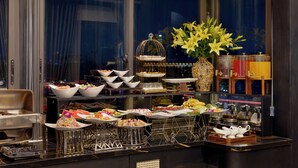 A buffet with various food items and a decorative vase of flowers. - Ja Cosmo Premier Hotel (Hanoi)
