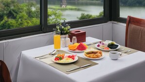 Une table dressée pour le petit-déjeuner, un verre de jus d’orange et une vue sur une rivière et la verdure environnante.