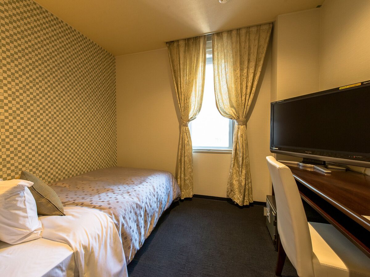 Une chambre d’hôtel comprenant un lit, un bureau avec un téléviseur à écran plat, une fenêtre avec des rideaux et un mur décoré d’un motif.