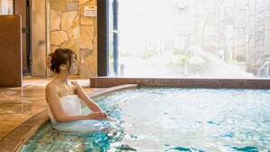 Eine Person entspannt in einem Thermalbad mit Steinmauern und Blick auf einen Garten.