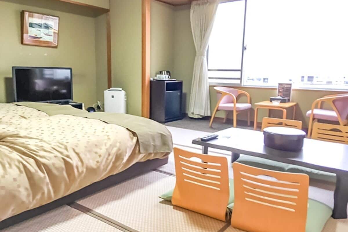 A hotel room with a bed, a desk, chairs, a television, and a window with curtains.