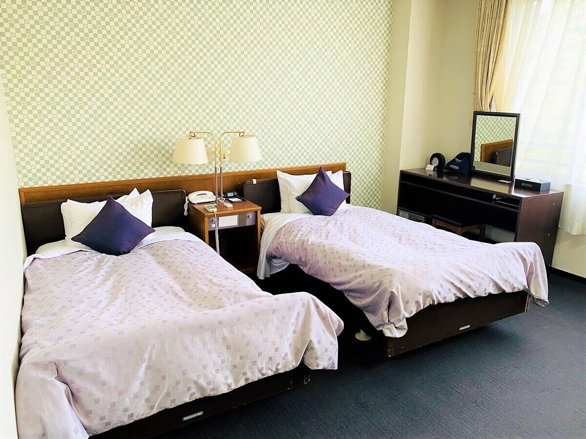 Une chambre d’hôtel avec deux lits, un bureau équipé d’un ordinateur, une lampe et un miroir.