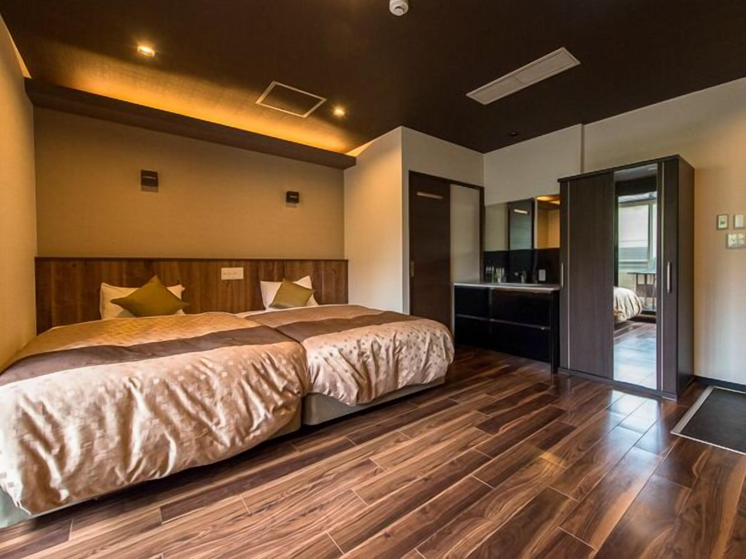 A modern hotel room with a large bed, wooden flooring, a desk, and a mirror.