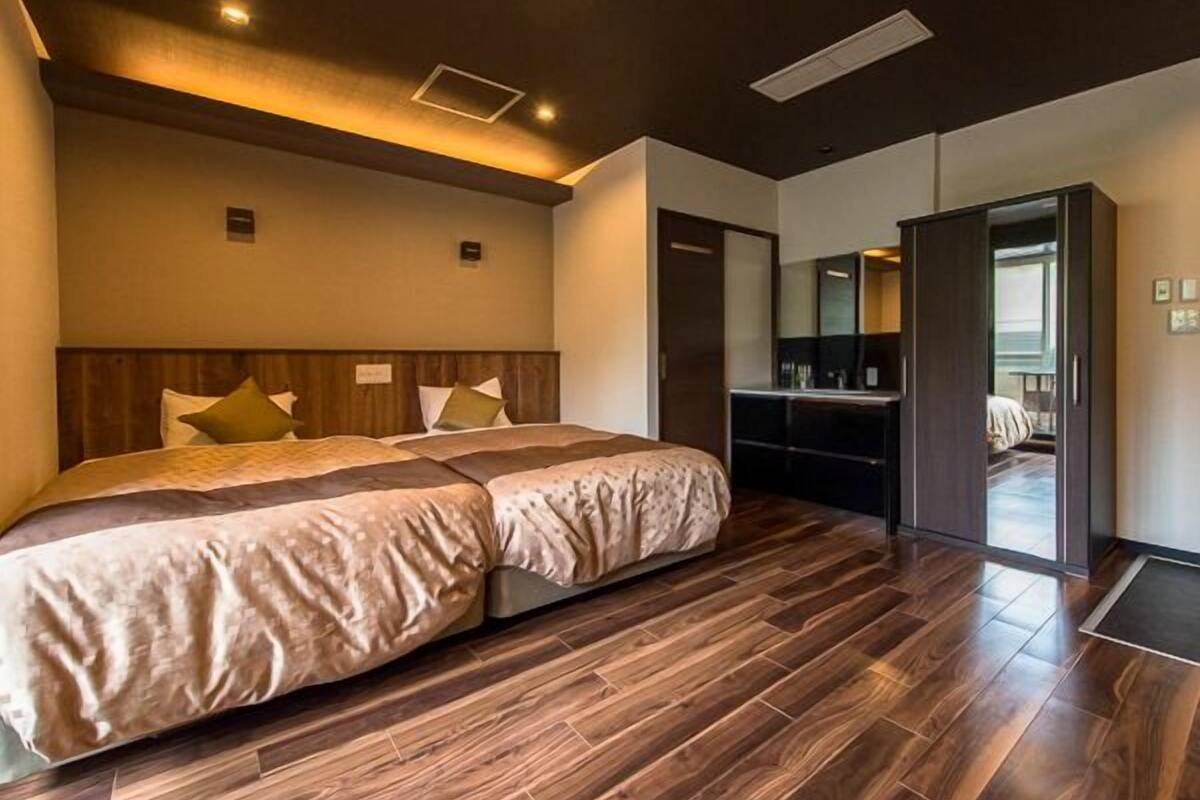 A modern hotel room with a large bed, wooden flooring, a desk, and a mirror.