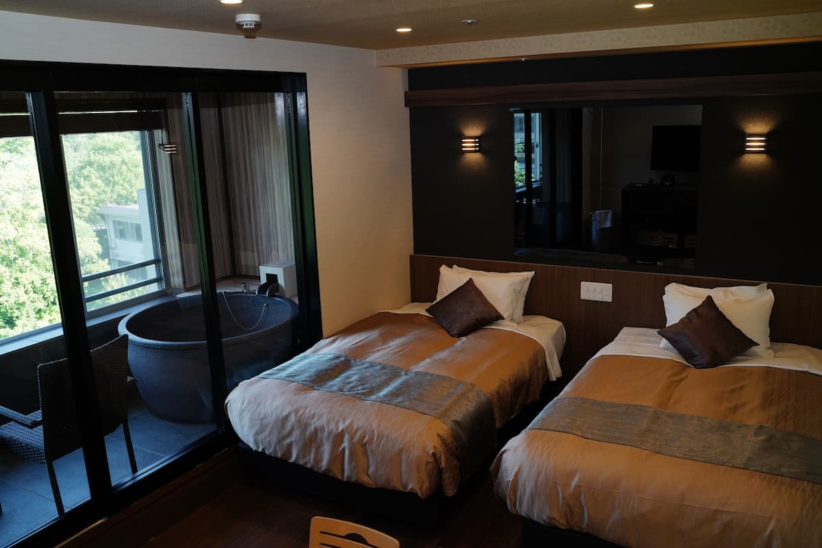A hotel room with two beds, a large bathtub, and a sliding glass door leading to a balcony.