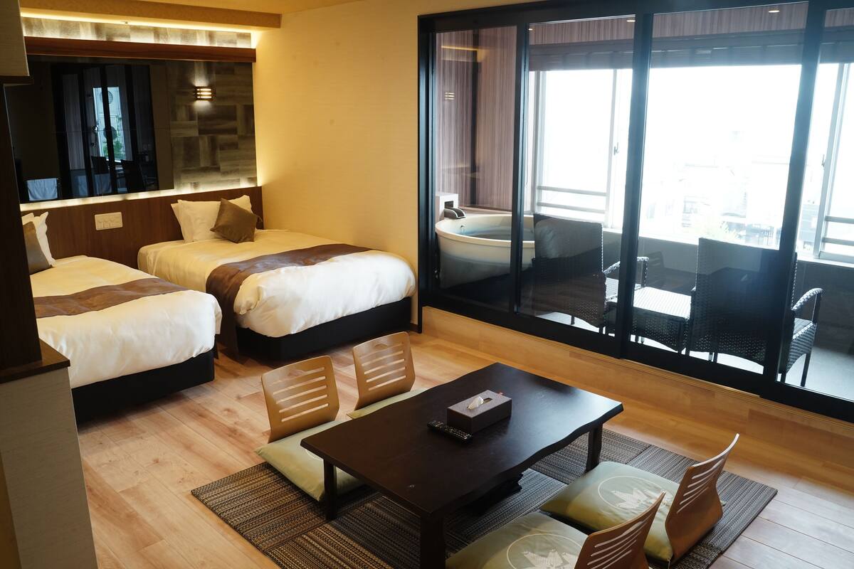 A hotel room with two beds, a sofa, a coffee table, and a large window with a view of the outside.