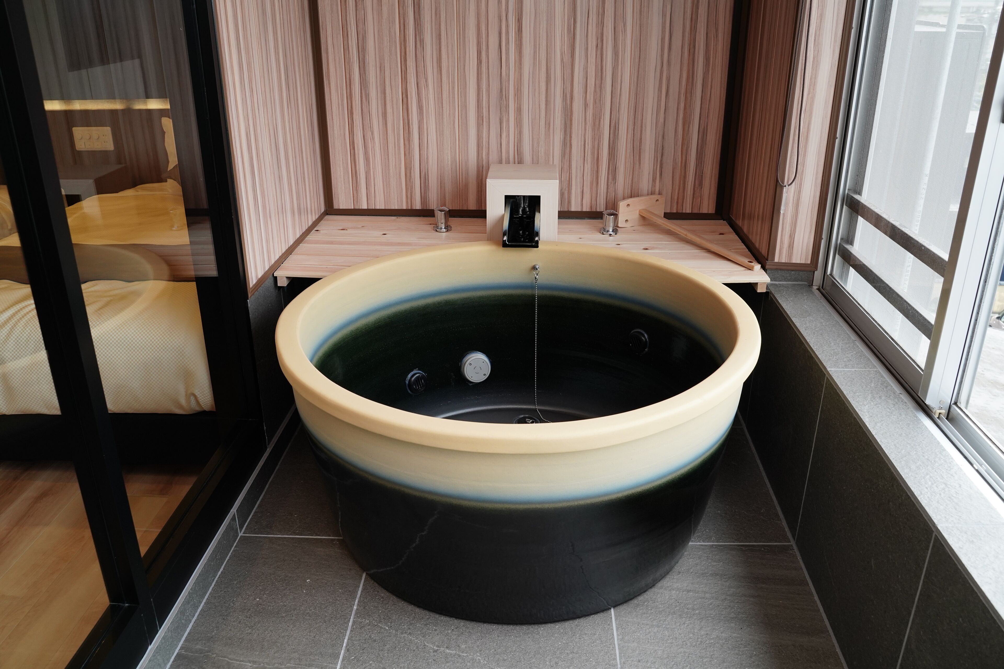 A modern bathroom with a large bathtub, a small table with a device, and a window.