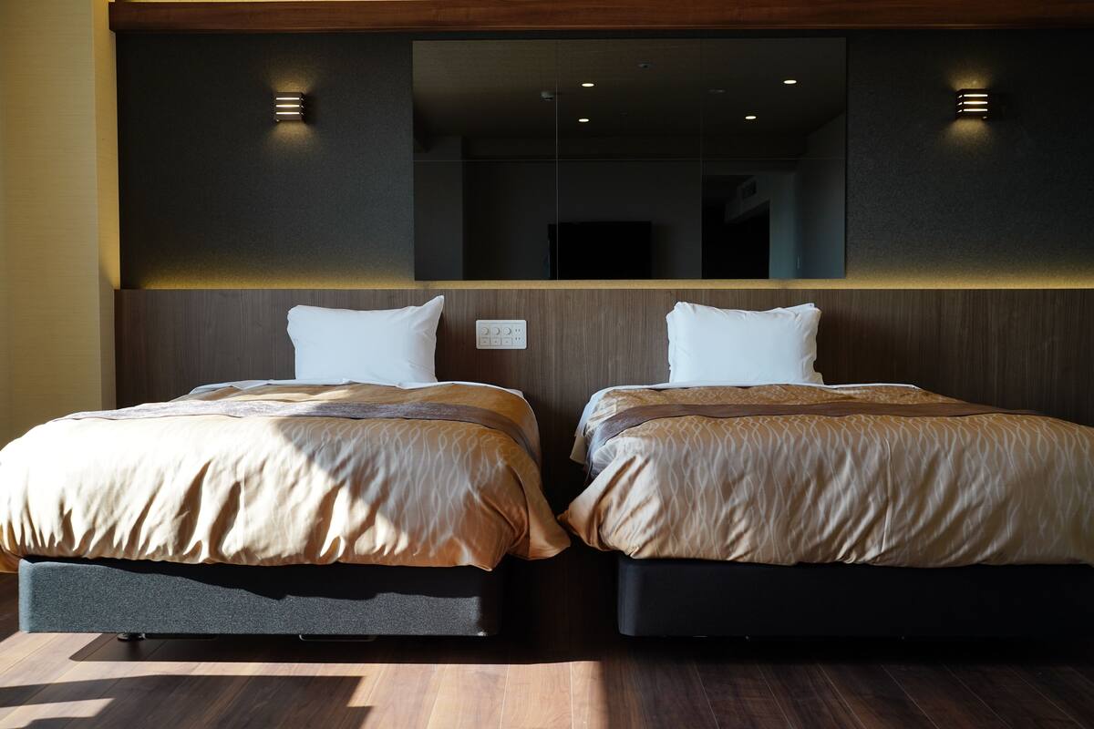 A hotel room with two beds, each with a pillow and a blanket.