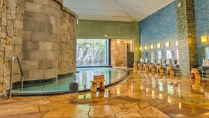 Ein Wellnessbereich mit einer Steinsäule, einem Pool und Holzliegen.