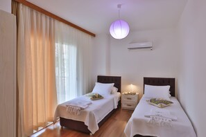 Habitación de hotel con dos camas individuales, una mesita de noche con lámpara, una lámpara de techo y un equipo de aire acondicionado.