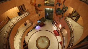 A grand atrium with a central fountain, multiple levels with glass railings, and decorative wall art. - Hotel Devi Grand (Reasi)