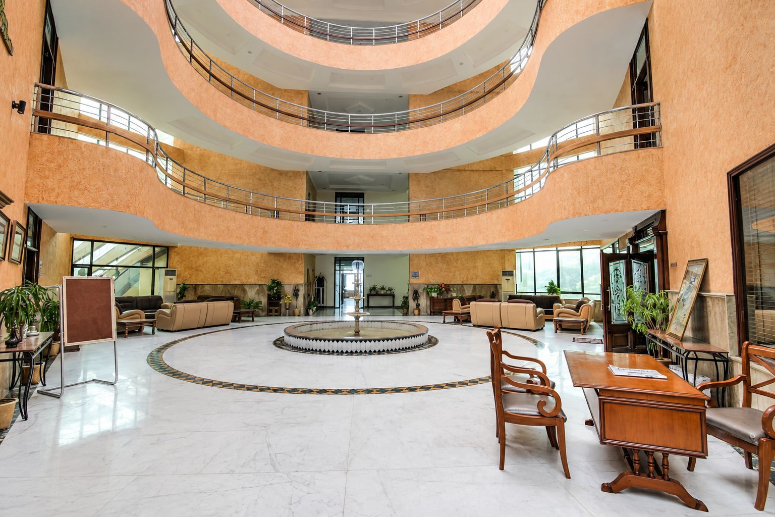 A spacious lobby with a central fountain, multiple seating areas, and a high ceiling with balconies.
