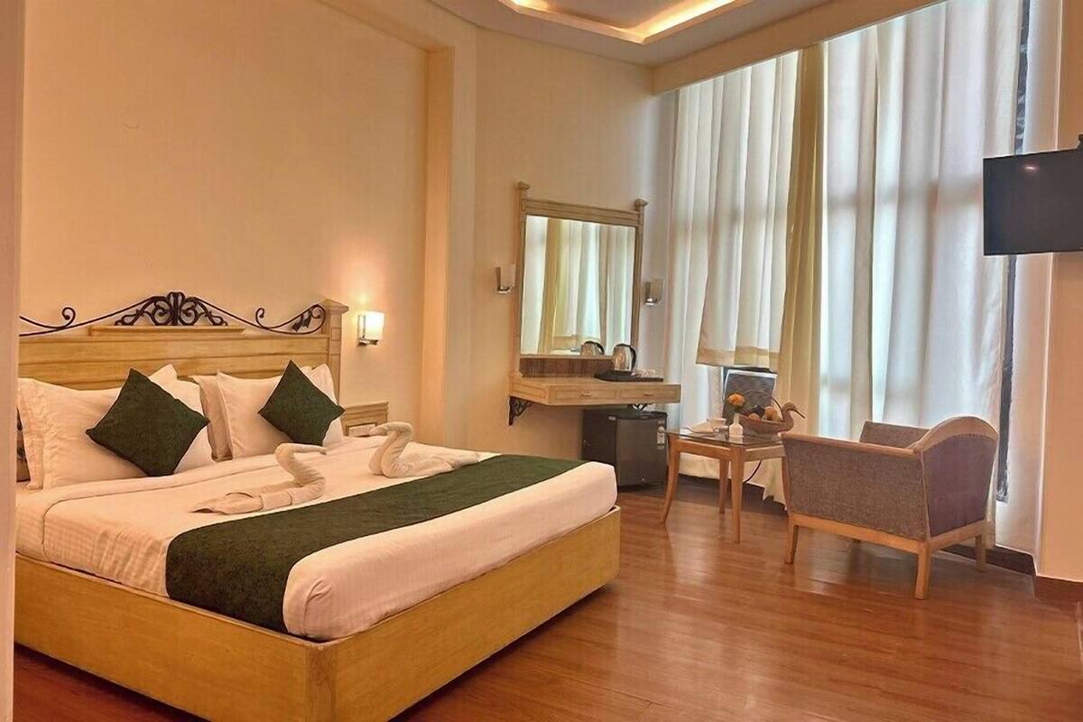 A hotel room with a large bed, a desk with a mirror, a chair, and a television on the wall.