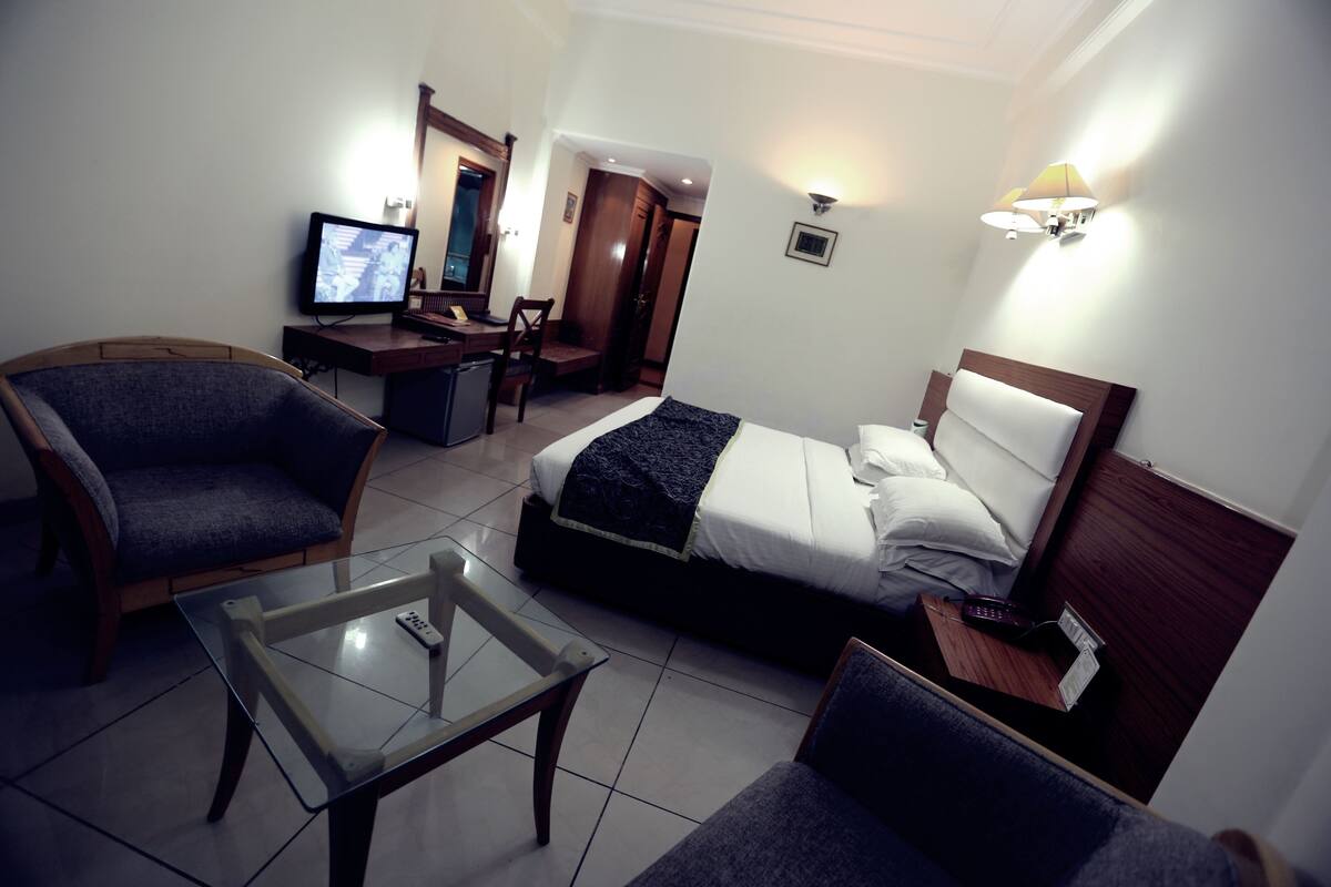 A hotel room with a bed, a desk, a chair, a TV, and a lamp.