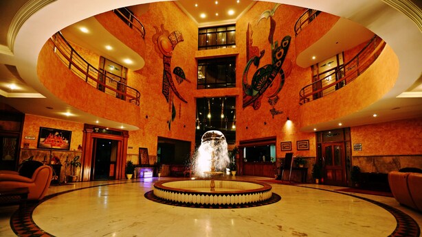 A lobby with a central fountain, multiple floors, and a circular seating area. - Hotel Devi Grand (Reasi)