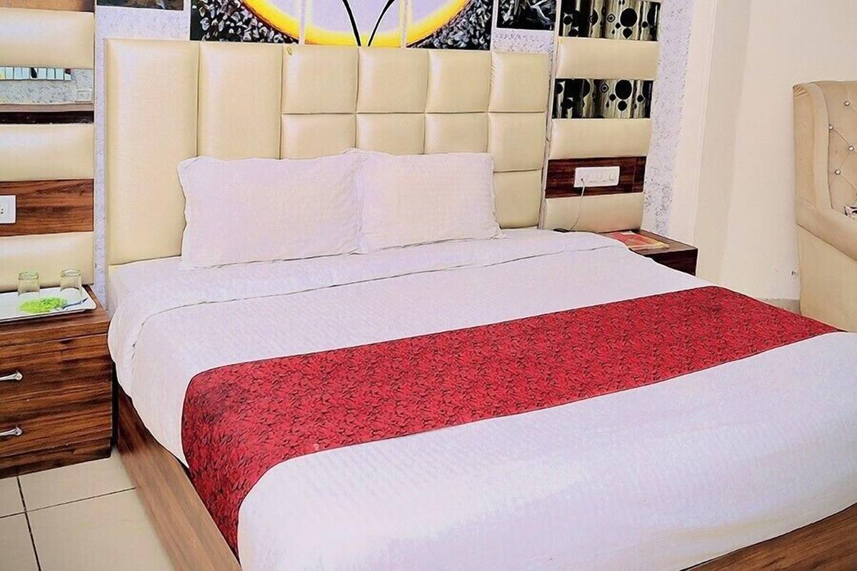 A neatly made bed with a red and white bedspread, a tufted headboard, and a bedside table with a lamp.