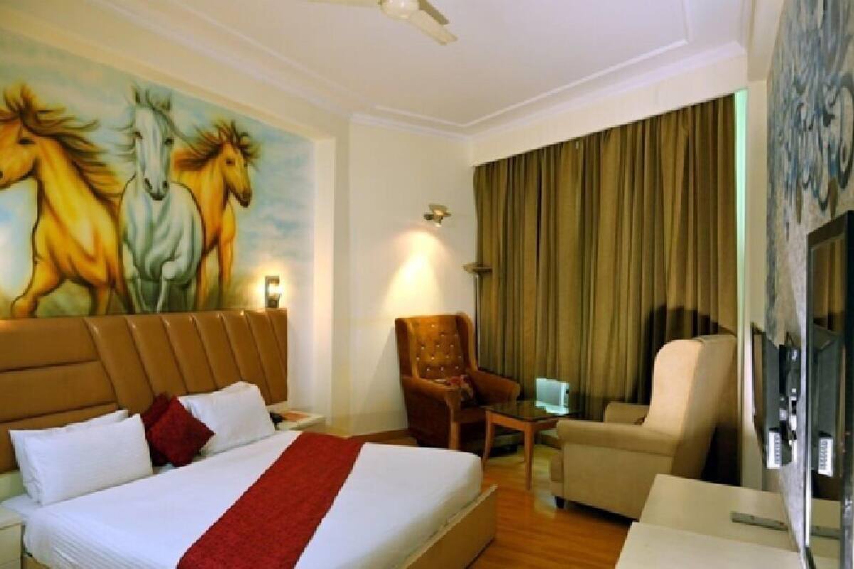 A hotel room with a large bed, two armchairs, a small table, and a painting of horses on the wall.