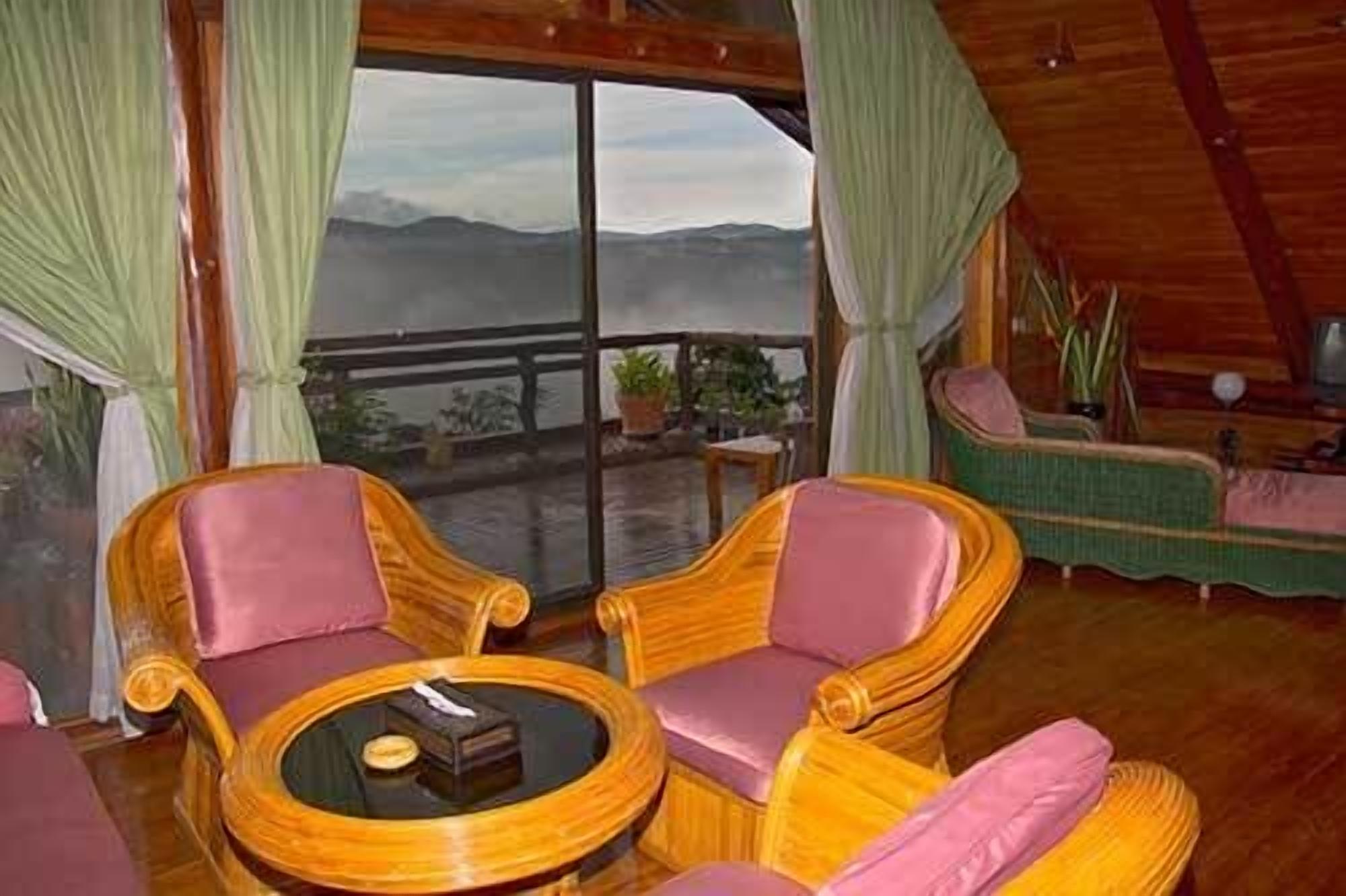 A cozy room with wicker furniture, a round table, and a view of mountains through large windows.