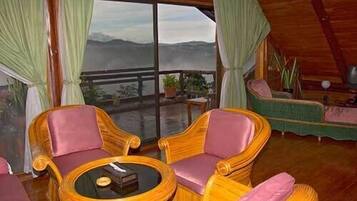 A cozy room with wicker furniture, a round table, and a view of mountains through large windows.