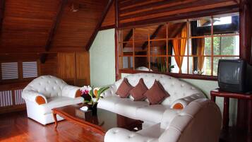 A spacious living room with a white sofa set, a wooden coffee table, and a television on a wooden stand.