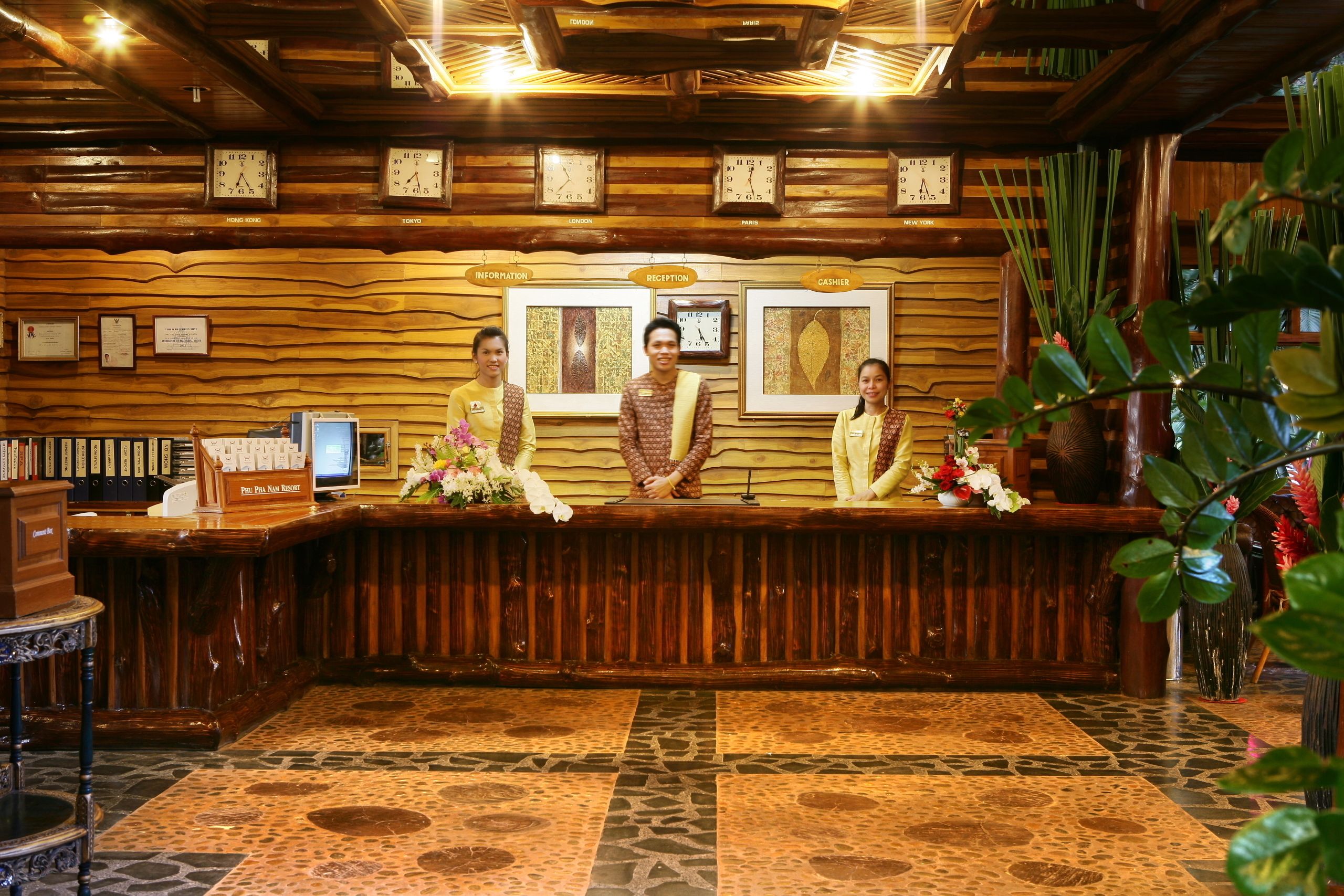 Una recepción con tres empleados, paneles de madera, relojes y obras de arte enmarcadas.