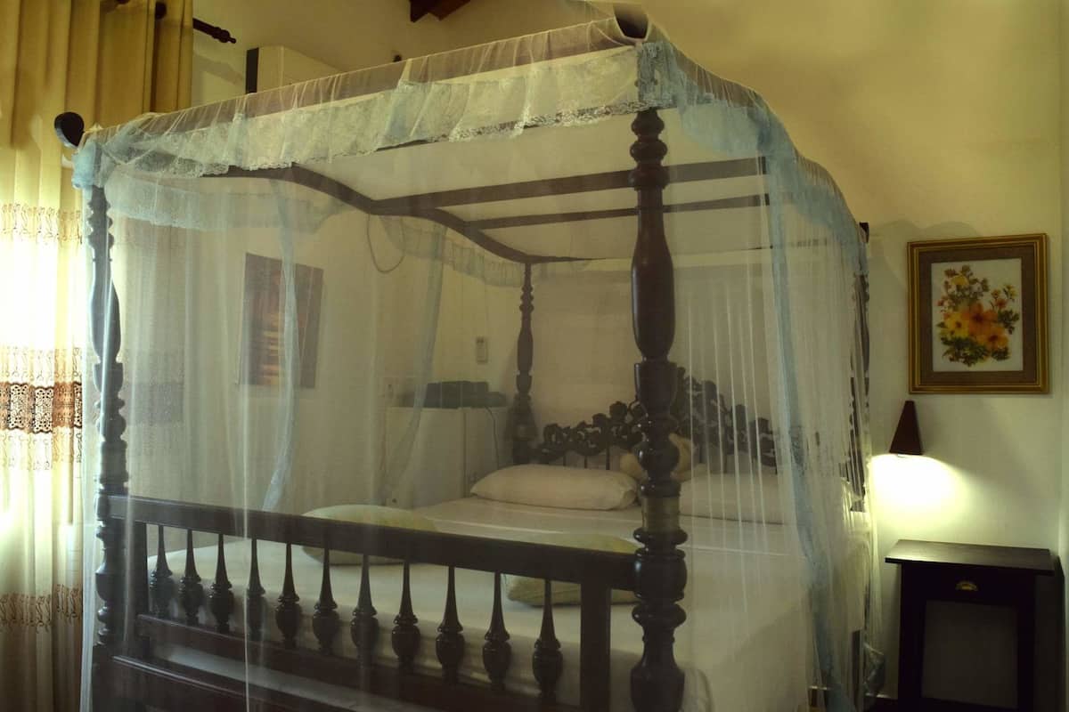 A four-poster bed with a canopy, a bedside table, and a framed floral picture on the wall.