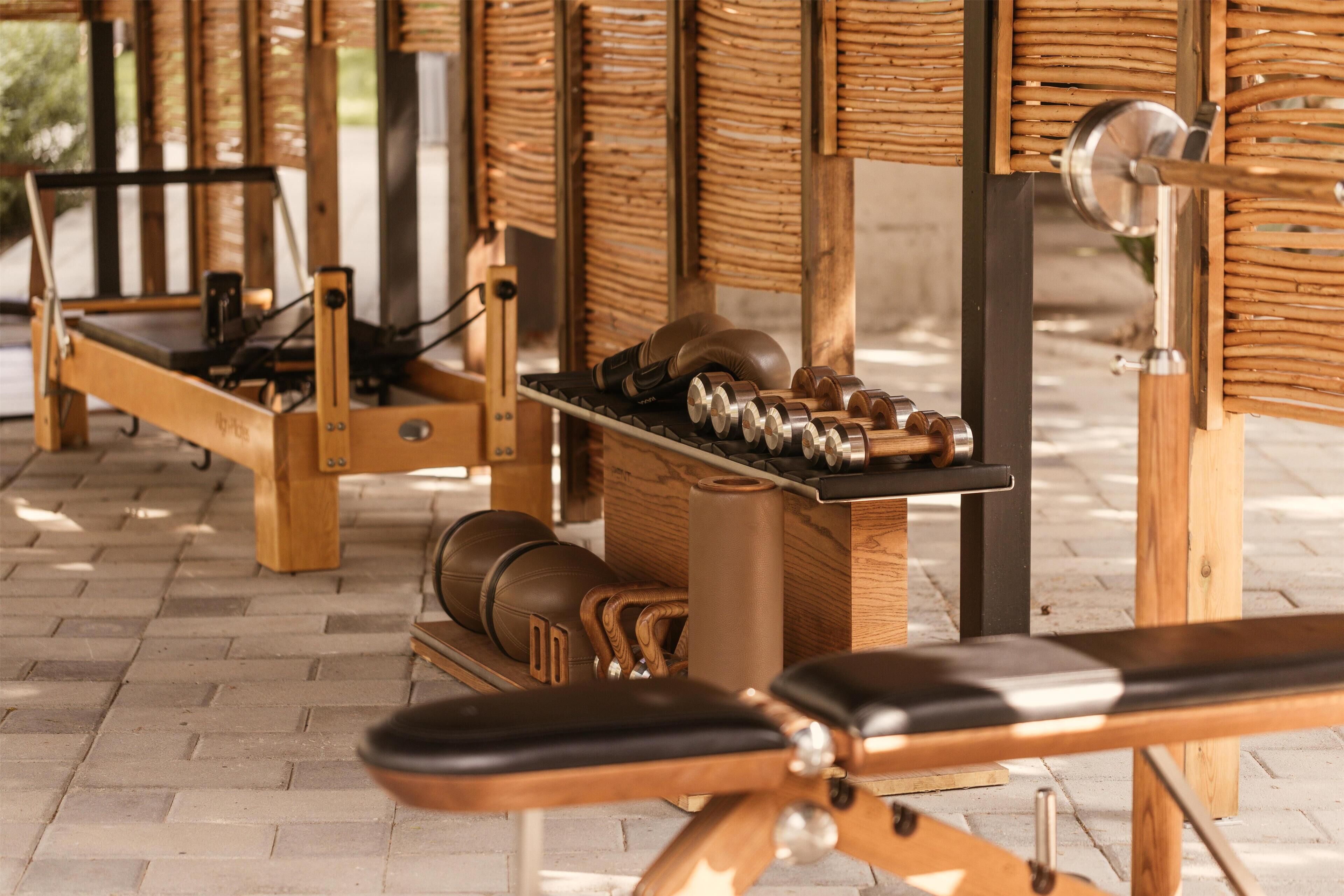 Una palestra con attrezzature da allenamento, tra cui panche e pesi, disposti in un ambiente aperto con pavimento in mattoni.