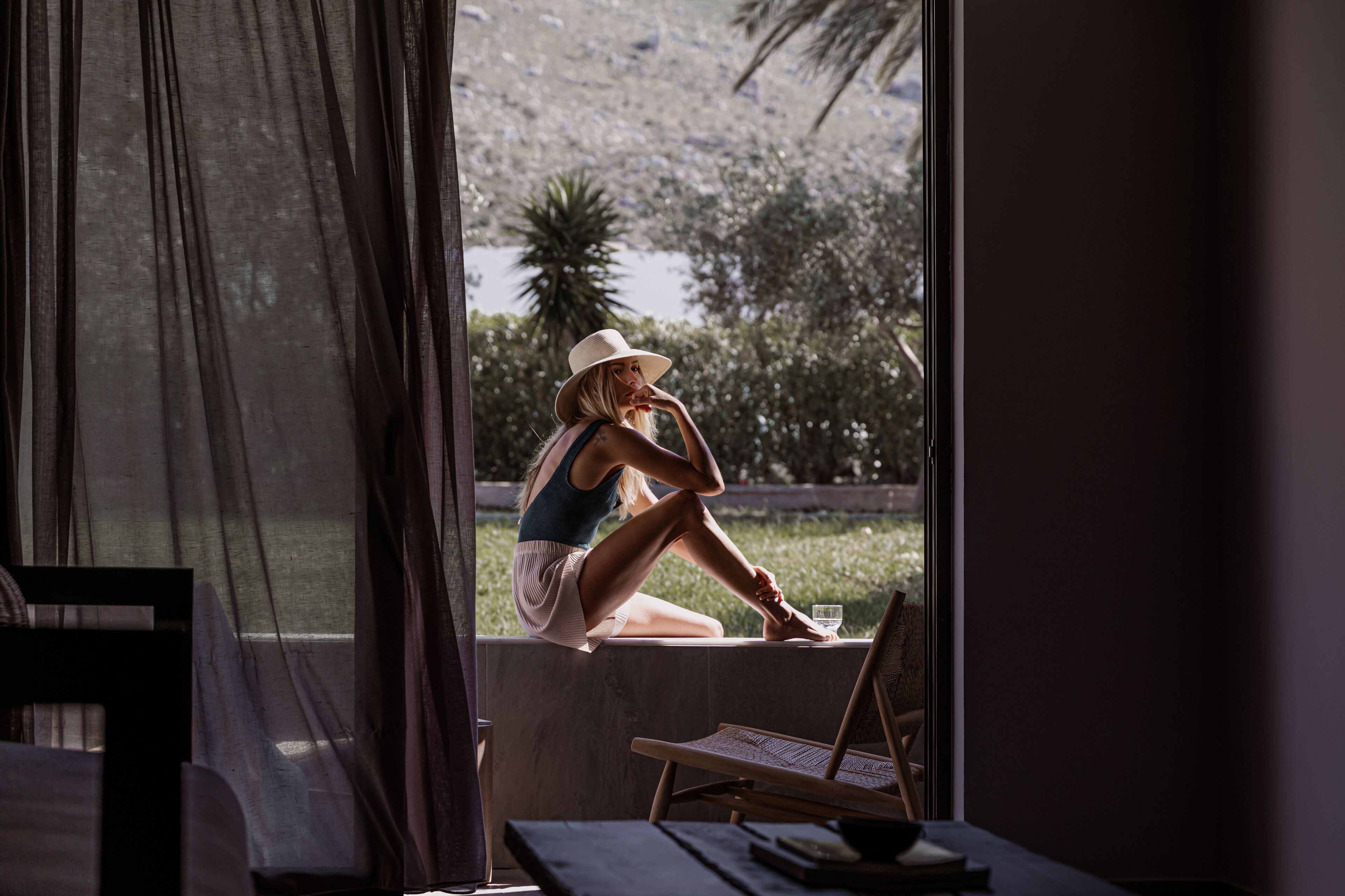 Una persona sentada junto a una ventana con vistas a follaje y una palmera.