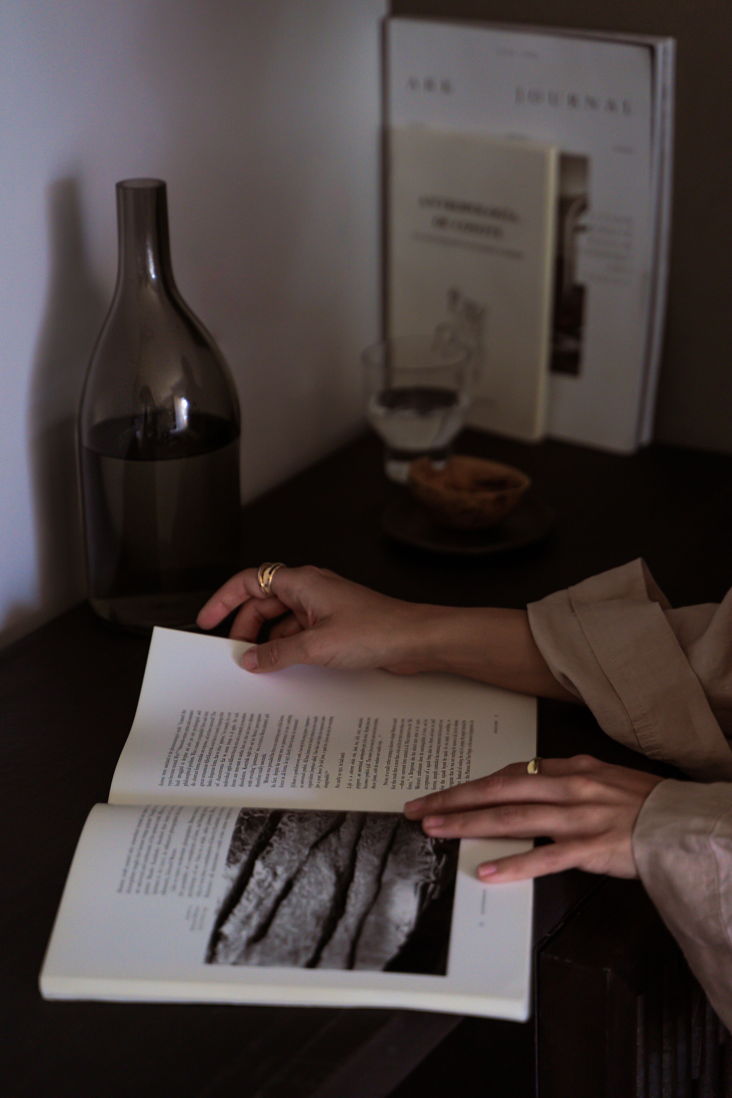 Una persona leyendo un libro con una vela y un cuenco sobre una mesa.