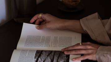 Una persona leyendo un libro con una vela y un cuenco sobre una mesa.