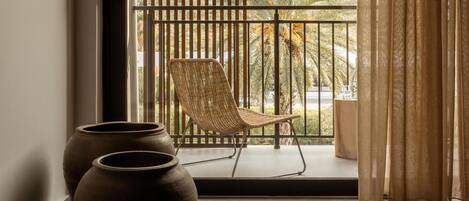 A balcony with a wicker chair and two vases, overlooking a landscape with trees and hills.