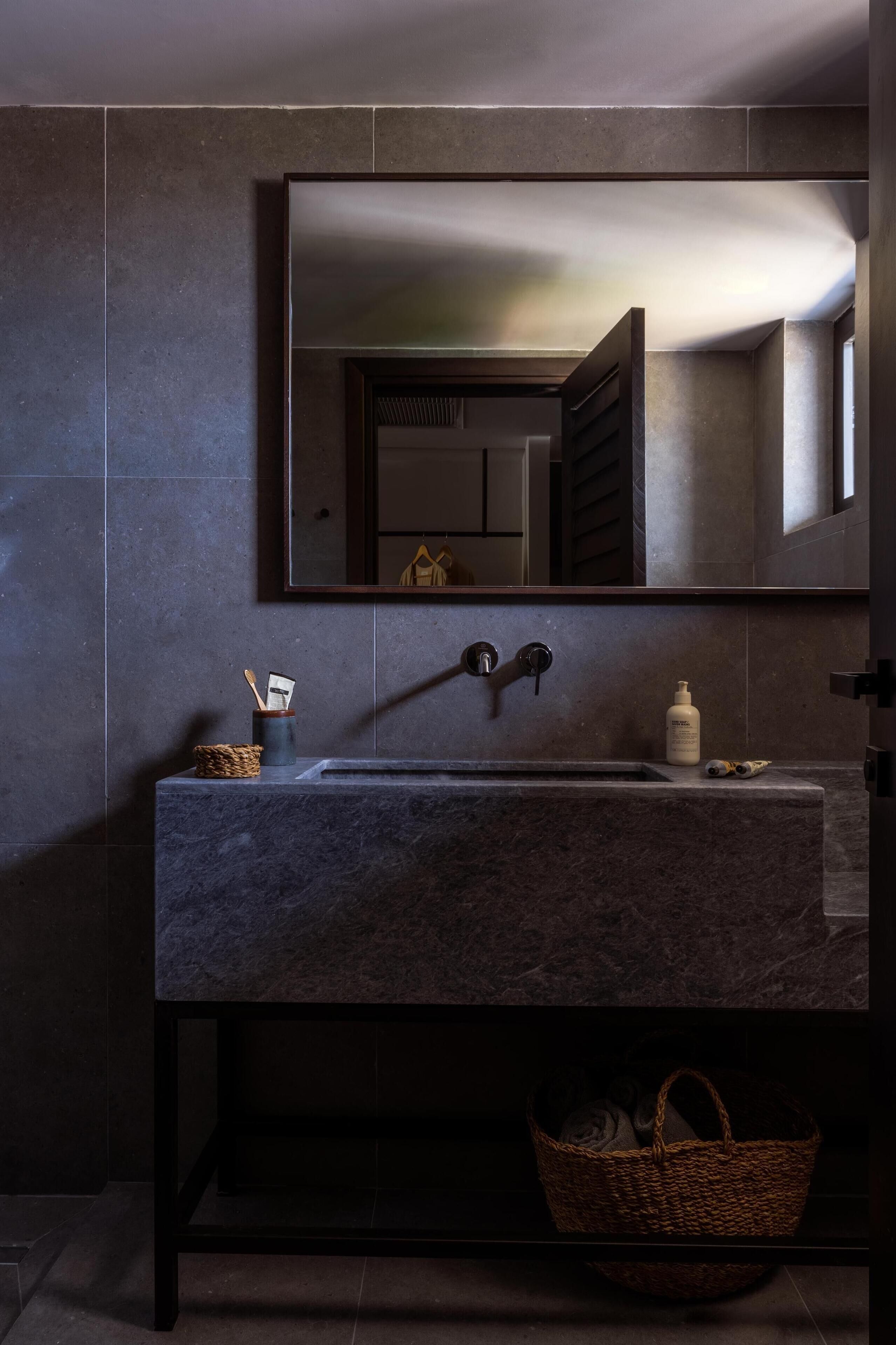 A modern bathroom with a dark marble sink, a large mirror, and a wicker basket below the counter.